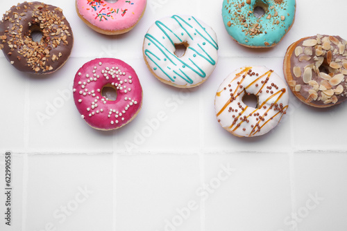 Different tasty donuts on white tiled table, flat lay. Space for text