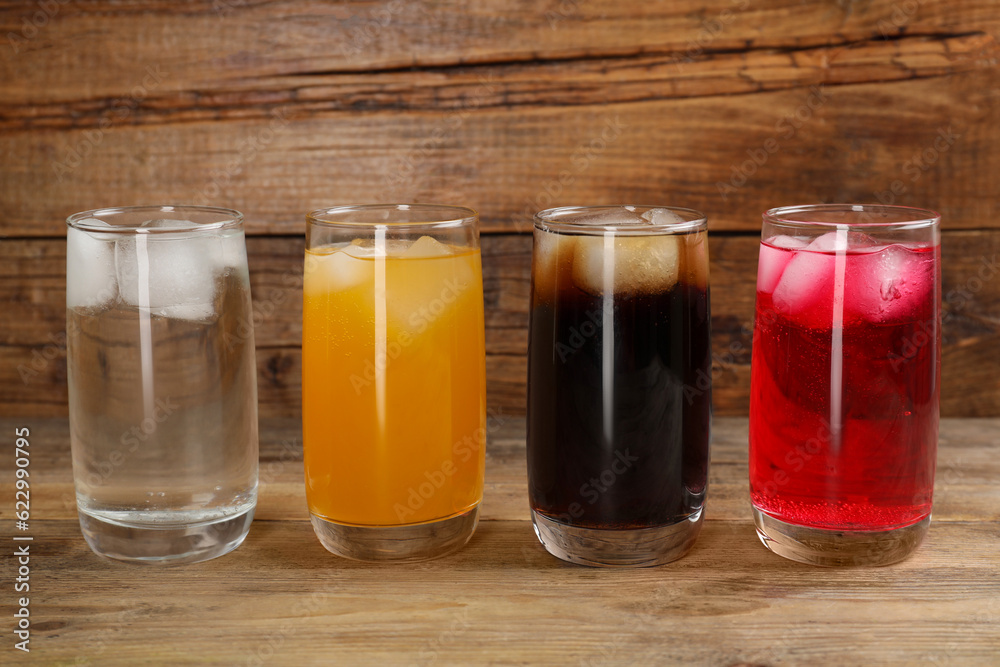 Glasses of different refreshing soda water with ice cubes on wooden table Glasses of different refreshing soda water with ice cubes on wooden table