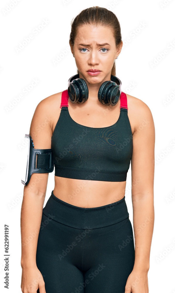 Beautiful blonde woman wearing gym clothes and using headphones skeptic and nervous, frowning upset because of problem. negative person. Beautiful blonde woman wearing gym clothes and using headphones skeptic and nervous, frowning upset because of problem. negative person.