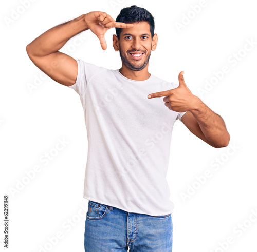 Young latin man wearing casual clothes smiling making frame with hands and fingers with happy face. creativity and photography concept.