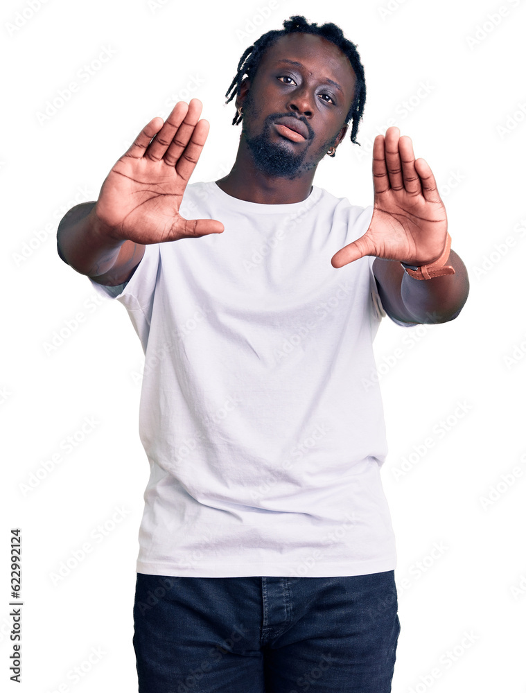 Fototapeta premium Young african american man with braids wearing casual white tshirt doing frame using hands palms and fingers, camera perspective