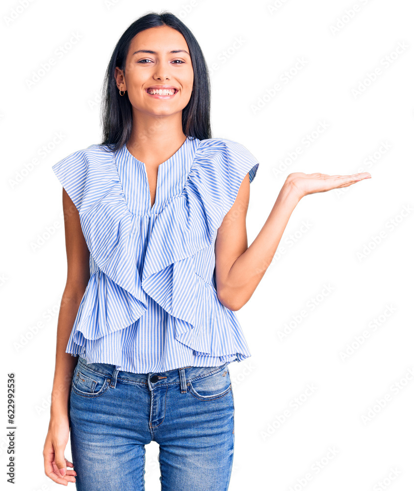 Young beautiful latin girl wearing casual clothes smiling cheerful presenting and pointing with palm of hand looking at the camera. Young beautiful latin girl wearing casual clothes smiling cheerful presenting and pointing with palm of hand looking at the camera.