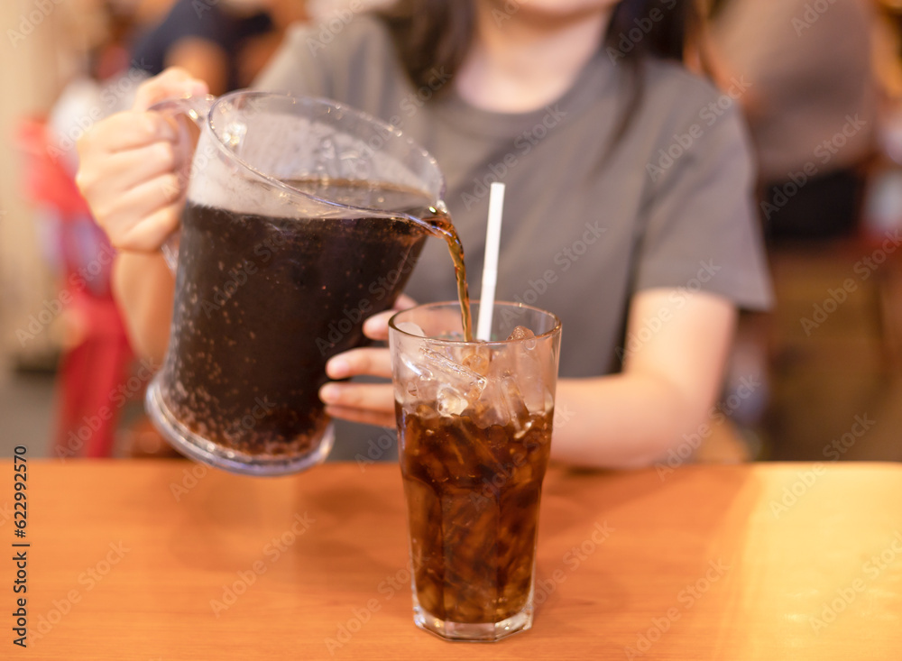 Woman pouring soft drink into glass in the restaurant. close-up the stream of cola is poured into a glass with ice on a dark. sugary drinks, Unhealthy diet, sweet sugary soft drinks, coke concept. Woman pouring soft drink into glass in the restaurant. close-up the stream of cola is poured into a glass with ice on a dark. sugary drinks, Unhealthy diet, sweet sugary soft drinks, coke concept.