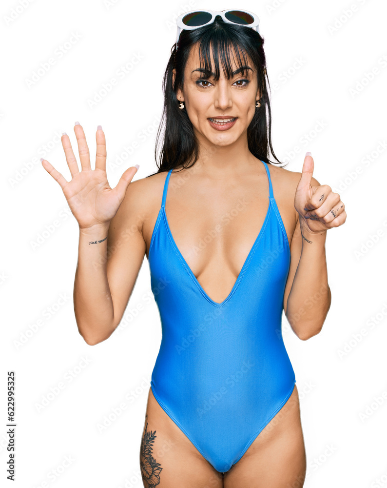 Young hispanic woman wearing swimsuit and sunglasses showing and pointing up with fingers number six while smiling confident and happy. Young hispanic woman wearing swimsuit and sunglasses showing and pointing up with fingers number six while smiling confident and happy.