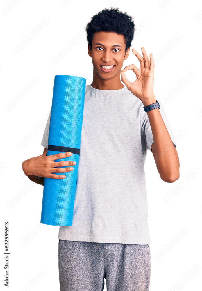 Young african american man holding yoga mat doing ok sign with fingers, smiling friendly gesturing excellent symbol Young african american man holding yoga mat doing ok sign with fingers, smiling friendly gesturing excellent symbol