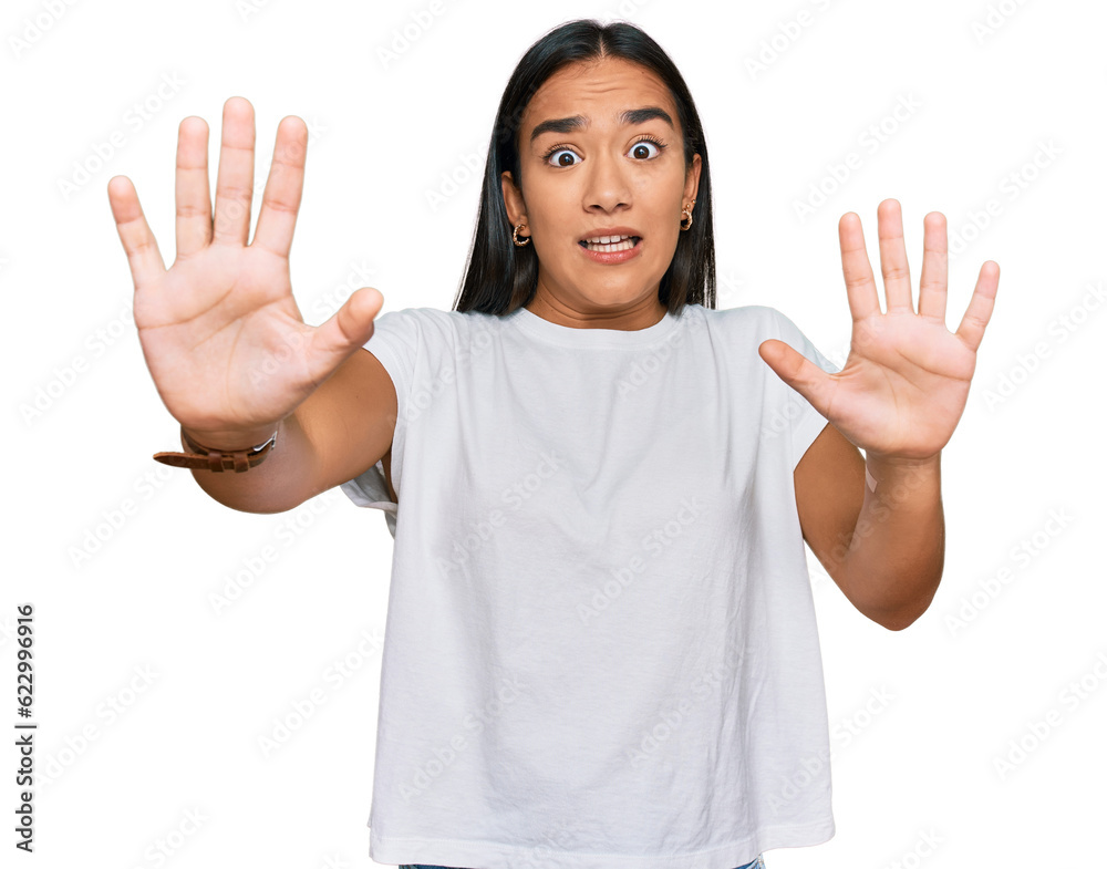 Young asian woman wearing casual white t shirt afraid and terrified with fear expression stop gesture with hands, shouting in shock. panic concept. Young asian woman wearing casual white t shirt afraid and terrified with fear expression stop gesture with hands, shouting in shock. panic concept.