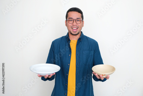 A man showing happy expression with one hand holding empty dinner plate and other hand holding empty bowl