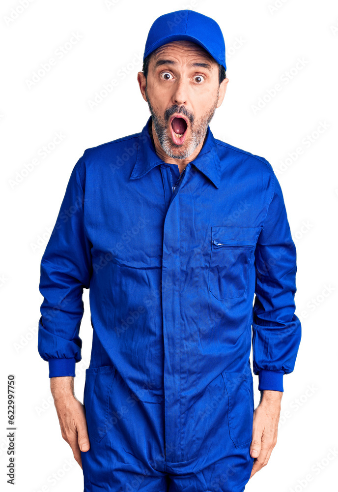 Middle age handsome man wearing mechanic uniform afraid and shocked with surprise and amazed expression, fear and excited face.