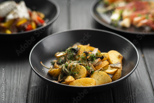 Fried potatoes with mushrooms and onions served on a black wooden background