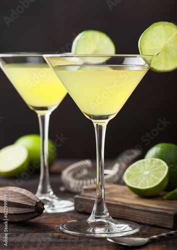 Gimlet Kamikaze cocktail in martini glasses with lime slice and ice on wood board with fresh limes and spoon.