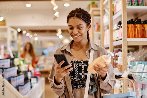 Young smiling customer using smartphone to buy cosmetics in shopping mall photo