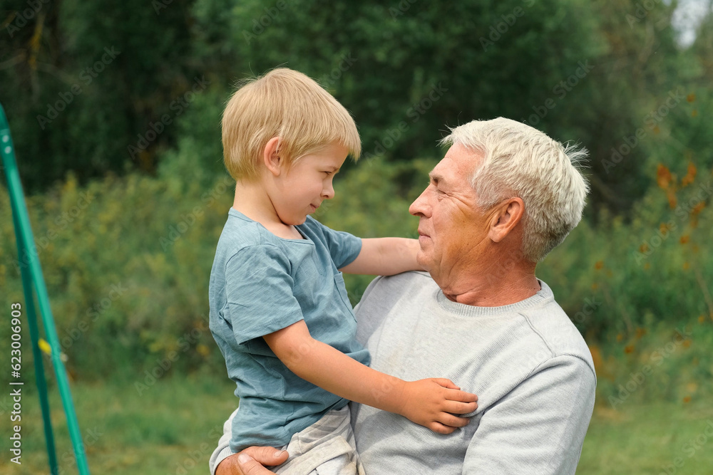 Fototapeta premium Grandfather and grandchild baby have fun during walk In Park. Happy family time. Old man grandpa hugging 4 years child boy at summer day. Smiling Senior male spending time with his grandson together.