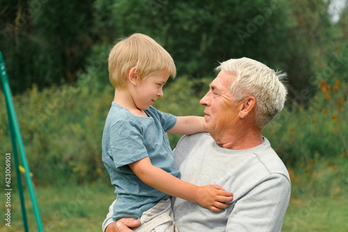 Grandfather and grandchild baby have fun during walk In Park. Happy family time. Old man grandpa hugging 4 years child boy at summer day. Smiling Senior male spending time with his grandson together.