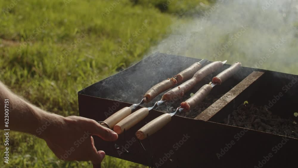 Man's hand turns over grilled sausages lying on the grill in the smoke. Man's hand turns over grilled sausages lying on the grill in the smoke.