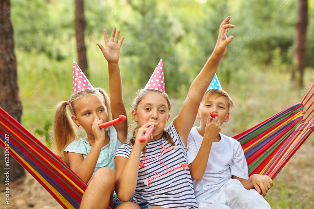 © Inna Vlasova - birthday, childhood and celebration concept - happy kids blowing party horns and having fun in summer outdoors