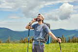 Handsome man standing in the meadow, making a call and laughing. Mountains on the background. Activity  and technology concept.