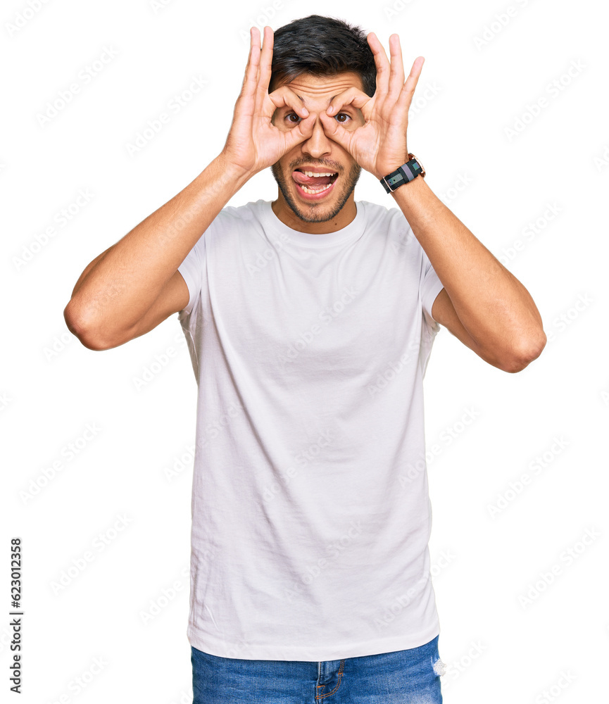 Young handsome man wearing casual white tshirt doing ok gesture like binoculars sticking tongue out, eyes looking through fingers. crazy expression. Young handsome man wearing casual white tshirt doing ok gesture like binoculars sticking tongue out, eyes looking through fingers. crazy expression.