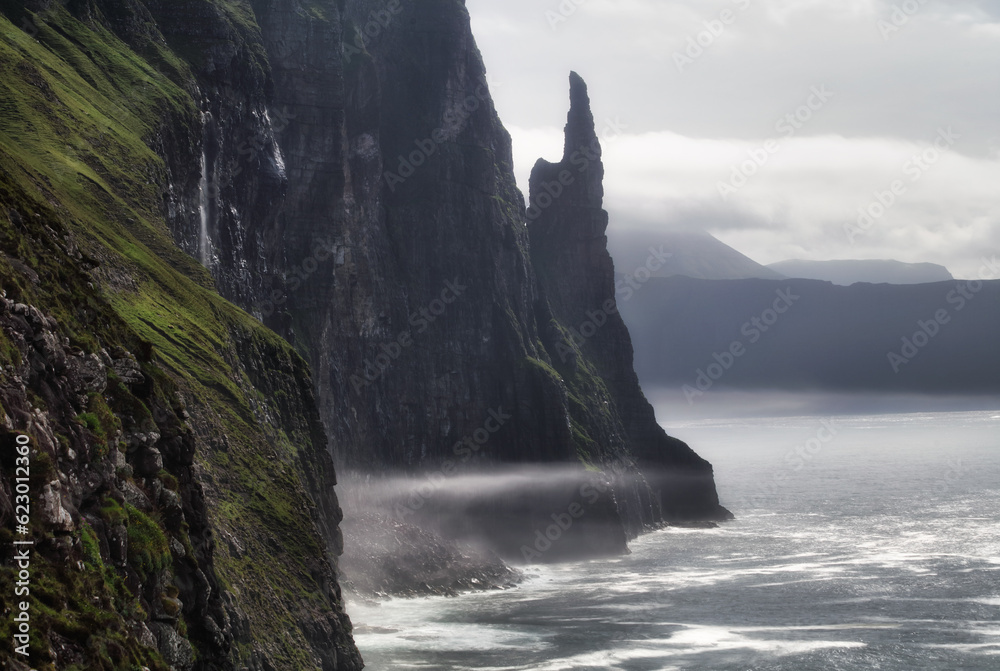 Rocky coastline and Trøllkonufingur otherwise known as The Troll Woman's Finger over at Vagar, Faroe Islands in the Atlantic Ocean.