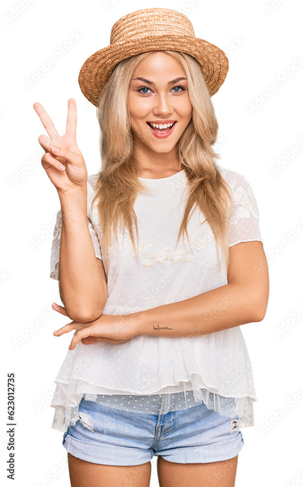 Young blonde girl wearing summer hat smiling with happy face winking at the camera doing victory sign. number two. Young blonde girl wearing summer hat smiling with happy face winking at the camera doing victory sign. number two.