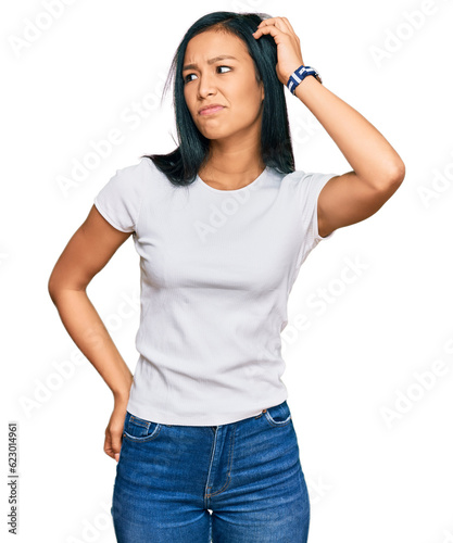 Beautiful hispanic woman wearing casual white tshirt confuse and wondering about question. uncertain with doubt, thinking with hand on head. pensive concept. photo