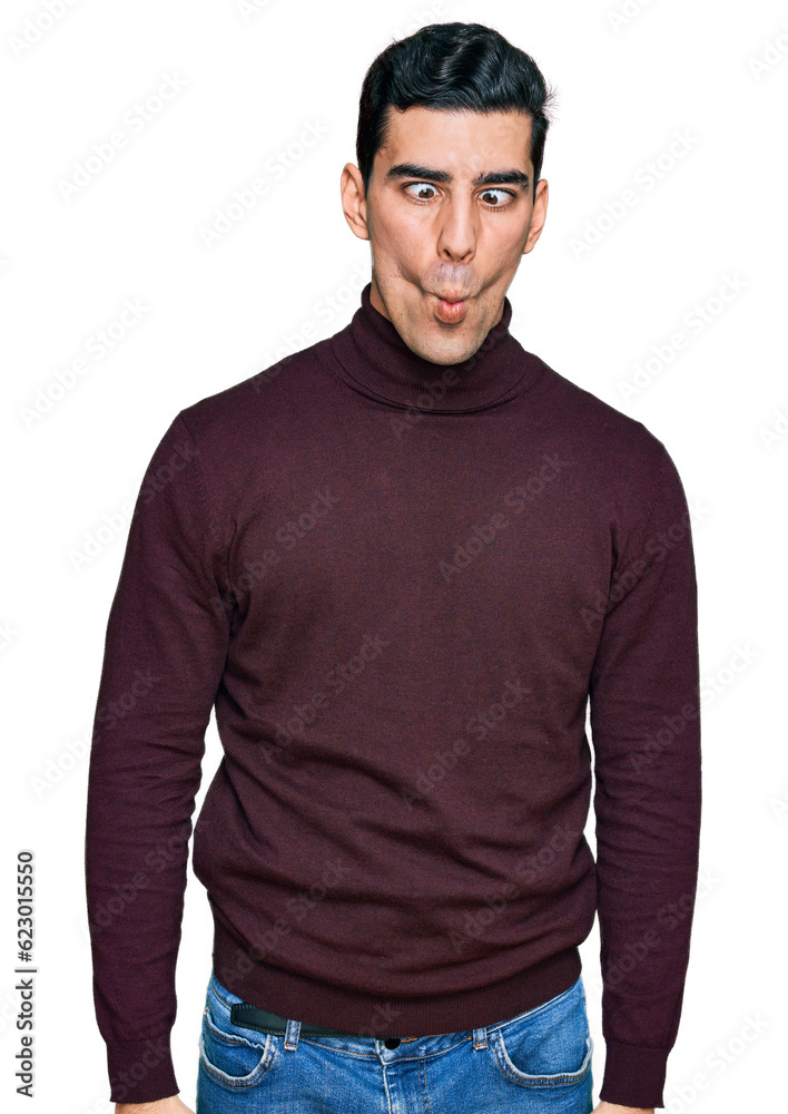 Handsome hispanic man wearing casual turtleneck sweater making fish face with lips, crazy and comical gesture. funny expression. Handsome hispanic man wearing casual turtleneck sweater making fish face with lips, crazy and comical gesture. funny expression.