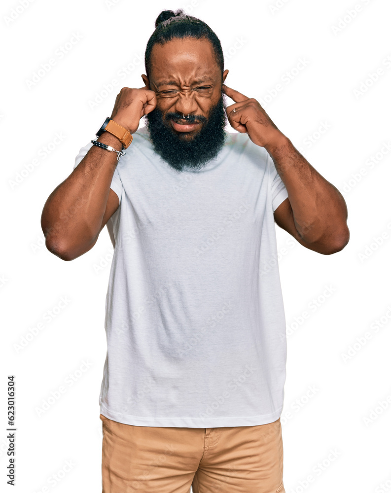 Young african american man wearing casual white tshirt covering ears with fingers with annoyed expression for the noise of loud music. deaf concept. Young african american man wearing casual white tshirt covering ears with fingers with annoyed expression for the noise of loud music. deaf concept.