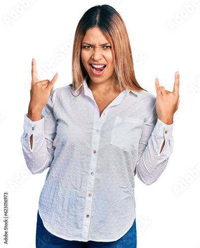 Young hispanic woman wearing casual white shirt shouting with crazy expression doing rock symbol with hands up. music star. heavy concept.