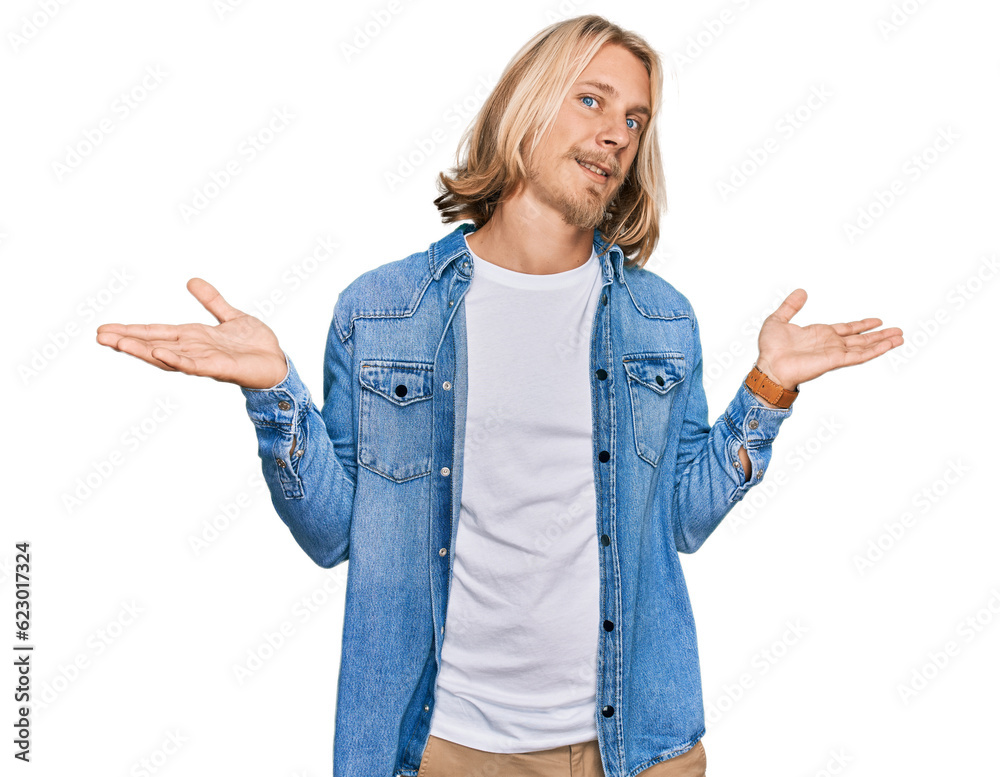 Caucasian man with blond long hair wearing casual denim jacket clueless and confused expression with arms and hands raised. doubt concept. Caucasian man with blond long hair wearing casual denim jacket clueless and confused expression with arms and hands raised. doubt concept.