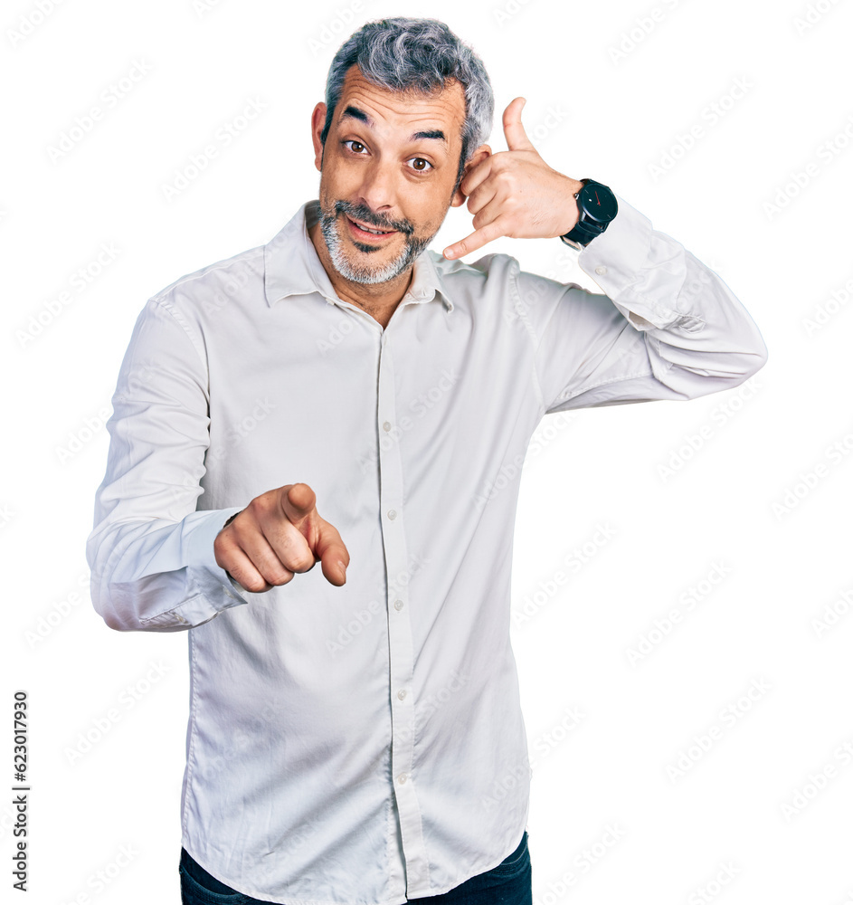 Middle age hispanic with grey hair wearing casual white shirt smiling doing talking on the telephone gesture and pointing to you. call me. Middle age hispanic with grey hair wearing casual white shirt smiling doing talking on the telephone gesture and pointing to you. call me.