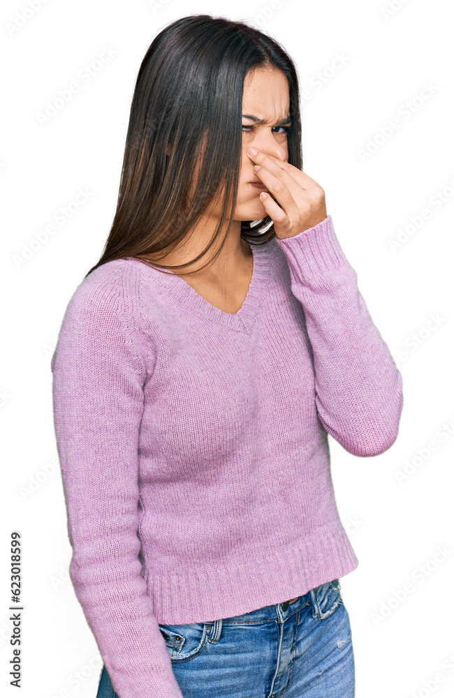 Young hispanic girl wearing casual clothes smelling something stinky and disgusting, intolerable smell, holding breath with fingers on nose. bad smell Young hispanic girl wearing casual clothes smelling something stinky and disgusting, intolerable smell, holding breath with fingers on nose. bad smell