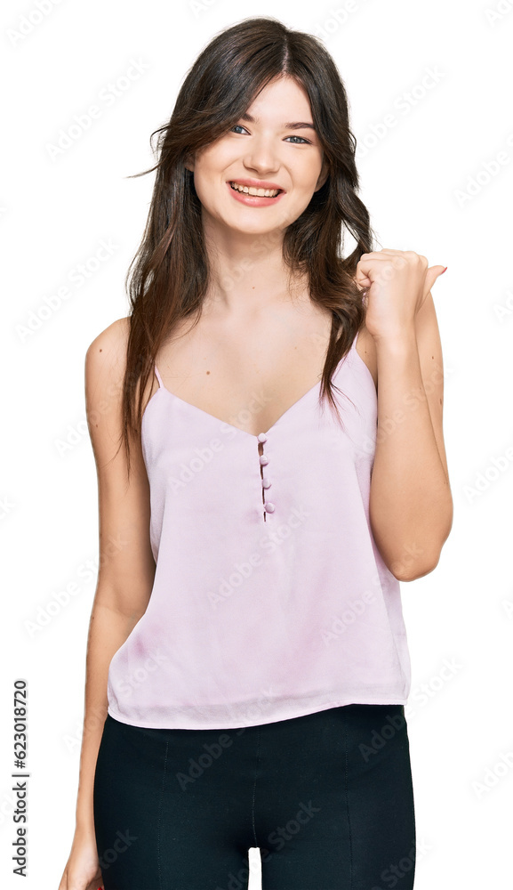 Young beautiful caucasian girl wearing casual clothes smiling with happy face looking and pointing to the side with thumb up. Young beautiful caucasian girl wearing casual clothes smiling with happy face looking and pointing to the side with thumb up.