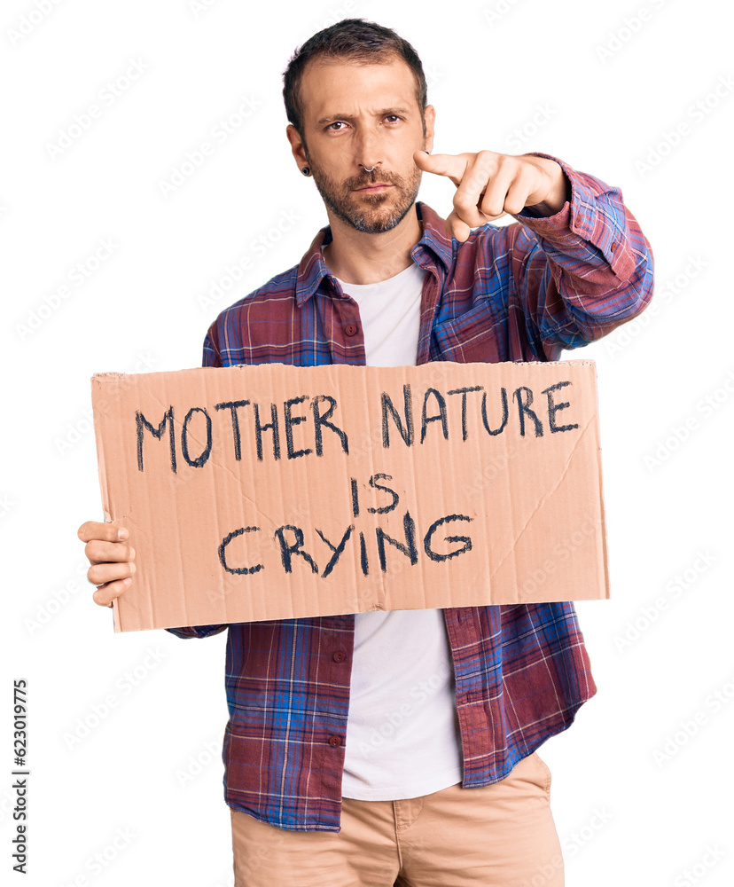 Young handsome man holding mother nature is crying protest cardboard banner pointing with finger to the camera and to you, confident gesture looking serious Young handsome man holding mother nature is crying protest cardboard banner pointing with finger to the camera and to you, confident gesture looking serious