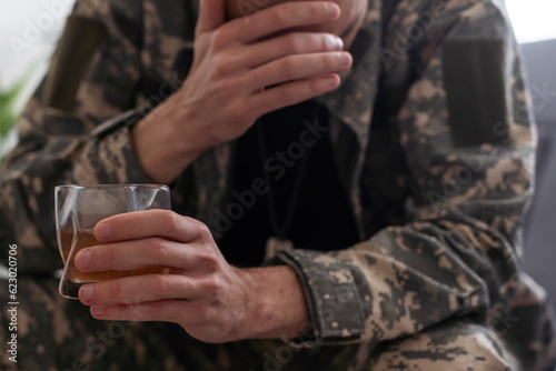 Depressed soldier with bottle sitting in livig room. Alcohol addiction. 