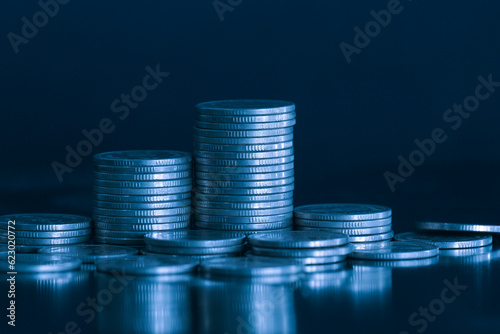 Money coin stack on office desk with blue filter. Business and finance concept.