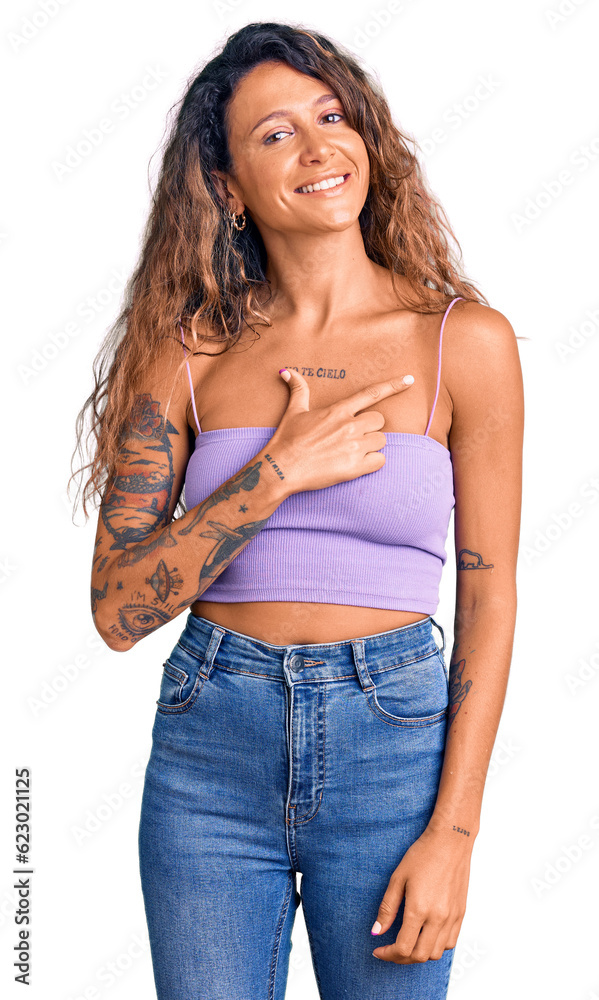Young hispanic woman with tattoo wearing casual clothes cheerful with a smile on face pointing with hand and finger up to the side with happy and natural expression Young hispanic woman with tattoo wearing casual clothes cheerful with a smile on face pointing with hand and finger up to the side with happy and natural expression