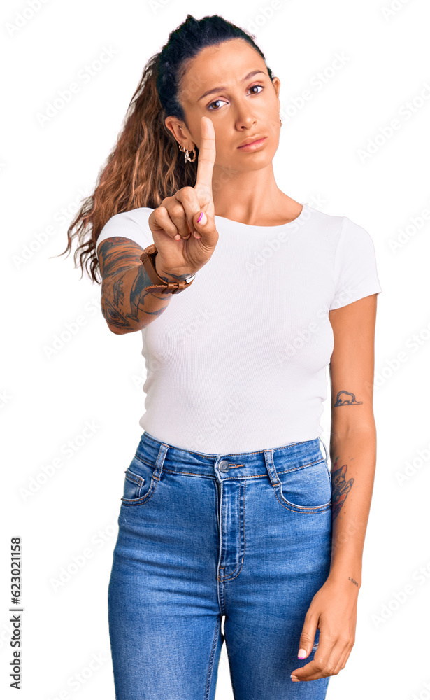 Young hispanic woman with tattoo wearing casual white tshirt pointing with finger up and angry expression, showing no gesture Young hispanic woman with tattoo wearing casual white tshirt pointing with finger up and angry expression, showing no gesture