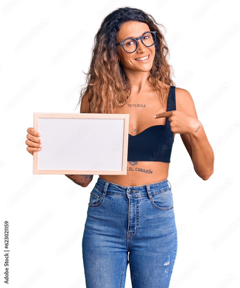 Young hispanic woman with tattoo holding empty white chalkboard pointing finger to one self smiling happy and proud Young hispanic woman with tattoo holding empty white chalkboard pointing finger to one self smiling happy and proud