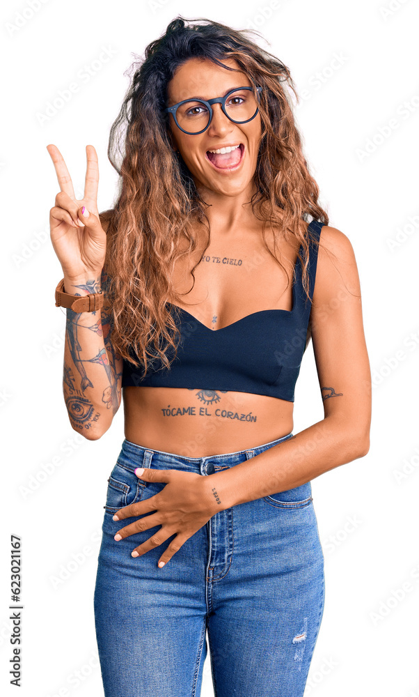 Young hispanic woman with tattoo wearing casual clothes and glasses smiling with happy face winking at the camera doing victory sign. number two. Young hispanic woman with tattoo wearing casual clothes and glasses smiling with happy face winking at the camera doing victory sign. number two.