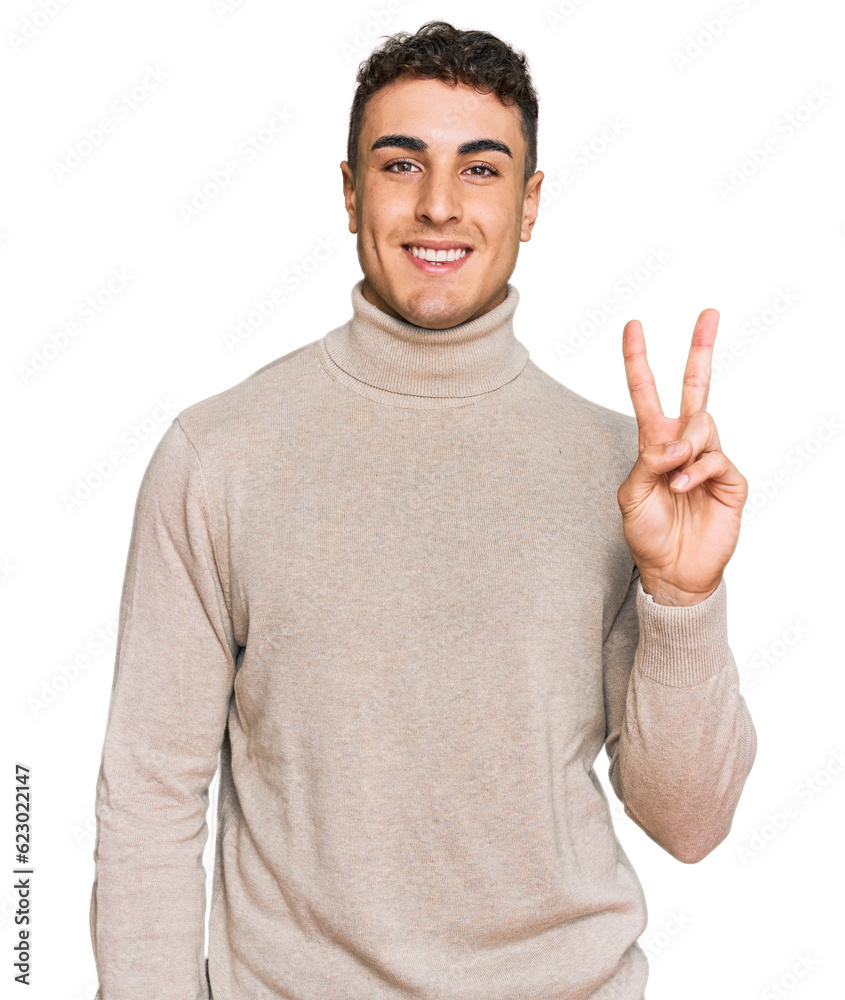 Naklejka premium Hispanic young man wearing casual turtleneck sweater smiling with happy face winking at the camera doing victory sign. number two.