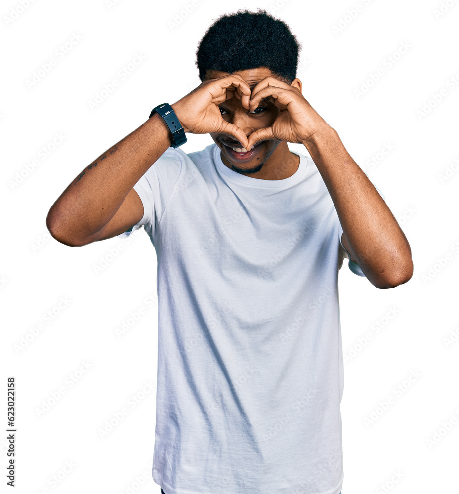 Young african american man wearing casual white t shirt doing heart shape with hand and fingers smiling looking through sign Young african american man wearing casual white t shirt doing heart shape with hand and fingers smiling looking through sign