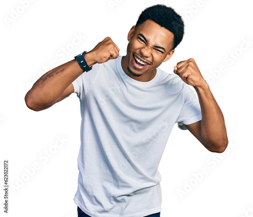 Young african american man wearing casual white t shirt angry and mad raising fists frustrated and furious while shouting with anger. rage and aggressive concept.