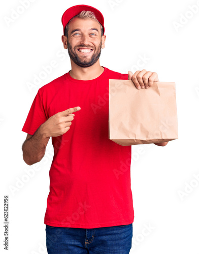 Obraz na plátně Young handsome blond man holding delivery paper bag smiling happy pointing with