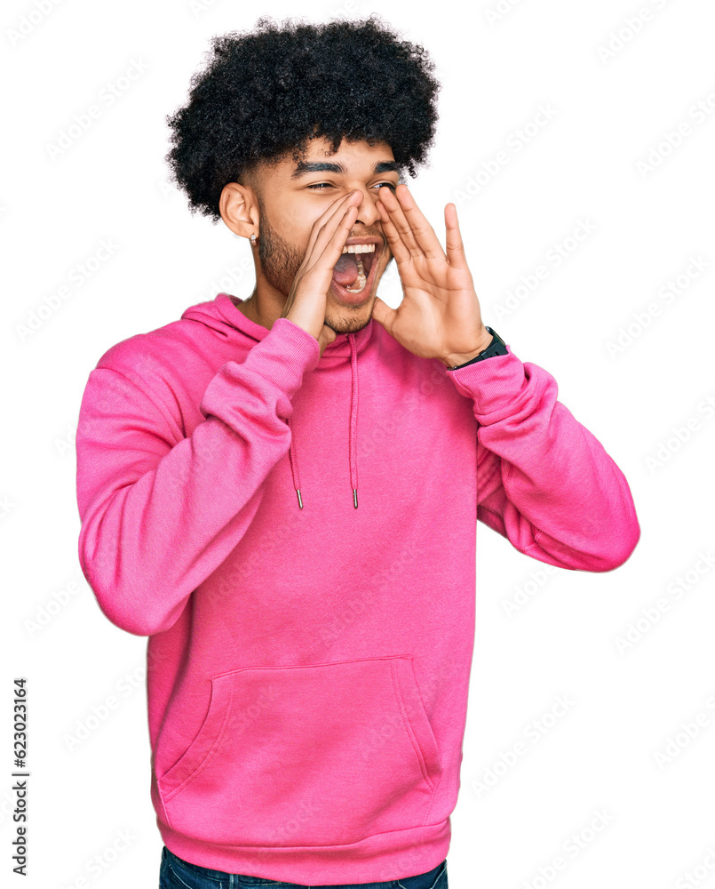 Young african american man with afro hair wearing casual pink sweatshirt shouting angry out loud with hands over mouth Young african american man with afro hair wearing casual pink sweatshirt shouting angry out loud with hands over mouth