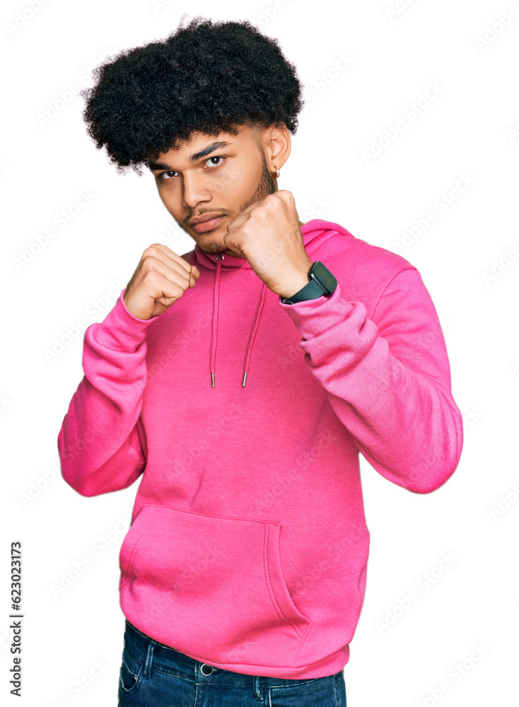 Young african american man with afro hair wearing casual pink sweatshirt ready to fight with fist defense gesture, angry and upset face, afraid of problem Young african american man with afro hair wearing casual pink sweatshirt ready to fight with fist defense gesture, angry and upset face, afraid of problem