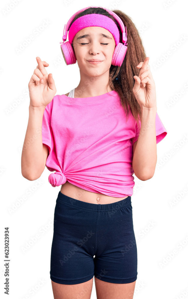 Cute hispanic child girl wearing gym clothes and using headphones gesturing finger crossed smiling with hope and eyes closed. luck and superstitious concept. Cute hispanic child girl wearing gym clothes and using headphones gesturing finger crossed smiling with hope and eyes closed. luck and superstitious concept.