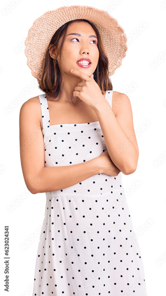 Young beautiful chinese girl wearing summer hat with hand on chin thinking about question, pensive expression. smiling with thoughtful face. doubt concept. Young beautiful chinese girl wearing summer hat with hand on chin thinking about question, pensive expression. smiling with thoughtful face. doubt concept.