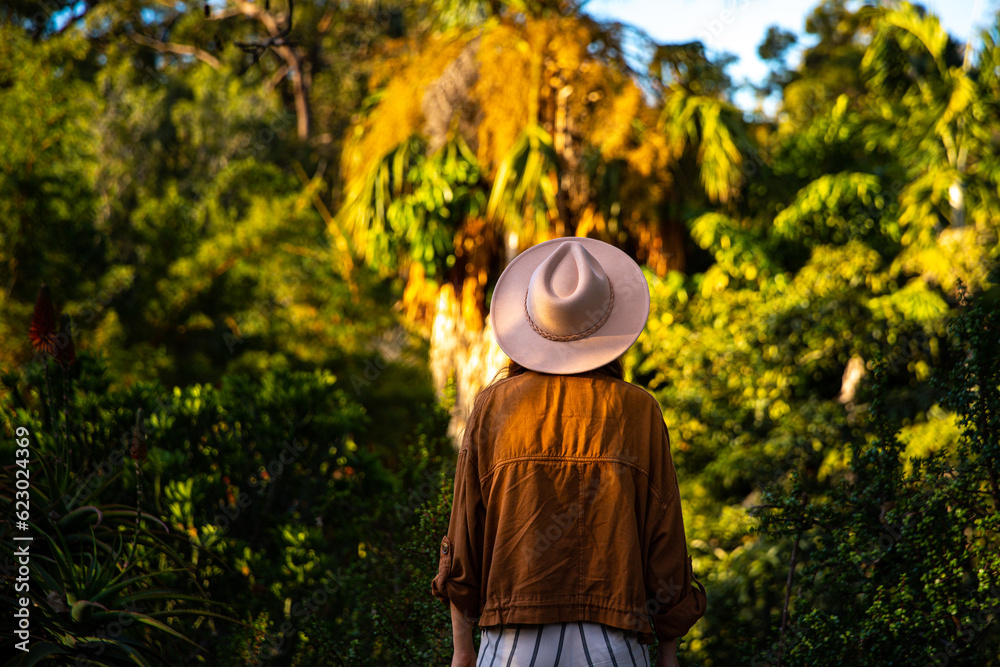 back view of pretty woman in a hat enjoying magical scenery of botanical garden in mount coot-tha, brisbane, queensland, australia; colorful sunset in a beautiful botanic gardens