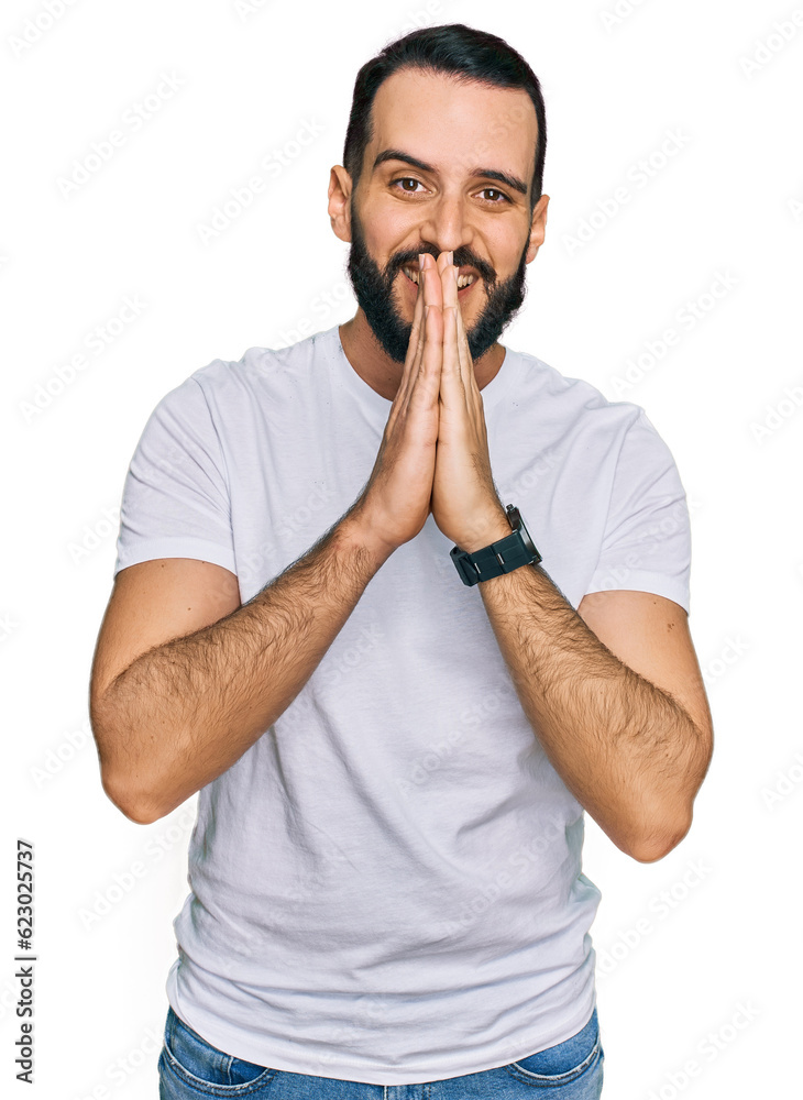 Young man with beard wearing casual white t shirt praying with hands together asking for forgiveness smiling confident. Young man with beard wearing casual white t shirt praying with hands together asking for forgiveness smiling confident.