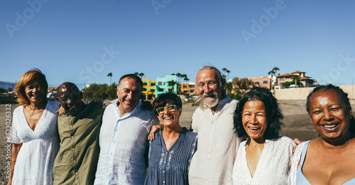 Happy senior people having fun walking on the beach at sunset wearing summer clothes - Joyful elderly lifestyle, pensioner vacation and travel concept - Main focus on center friends faces