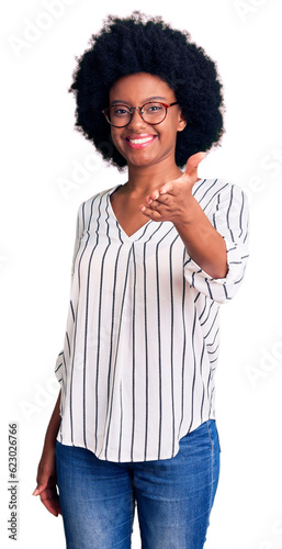 Young african american woman wearing casual clothes and glasses smiling friendly offering handshake as greeting and welcoming. successful business.